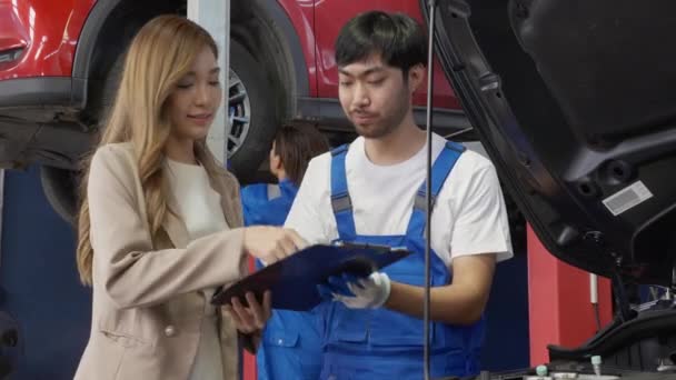 機械提供契約書顧客アジアの女性はガレージで修理と車について署名します 自動車サービス 技術者とクライアントは 車両の問題について合意を行います 輸送コンセプト — ストック動画