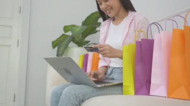 Young asian woman sitting on sofa using laptop computer shopping online with credit card buying to internet, happiness girl paying with transaction financial, purchase and payment, business concept.