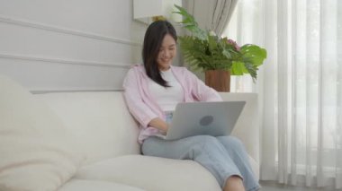 Young asian business woman work from home with laptop computer online to internet on sofa in living room, freelance girl using notebook sitting on couch with comfort and relax, lifestyles concept.