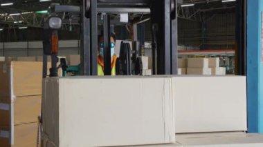 Genç Asyalı adam forklift kutusu kullanıyor ya da fabrikadaki depodaki konteynırlarda nakliye ve dağıtım için ambalaj yapıyor, depoda çalışan, lojistik ve nakliye konseptinde çalışan.