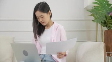 Young asian business woman working on laptop computer and looking graph and chart of report for profit on paper at home, businesswoman looking investment and income, data of infographic statistics.