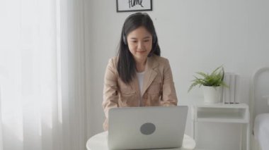 Young asian businesswoman wearing headset video call and explain conference online at home, woman wearing headphone meeting and talking for working from home, business and communication concept.
