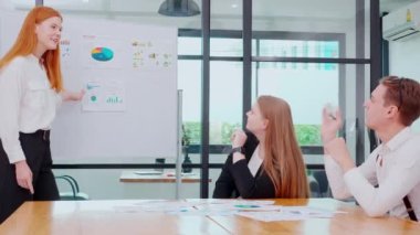 Grup iş adamları finans ve kâr hakkında pazarlama ile buluşurken, iş kadını da planlama ve beyin fırtınası için meslektaşlarıyla birlikte sunum ve grafikleri ve grafikleri beyaz tahtada açıklıyor..