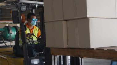 Genç Asyalı adam forklift kutusu kullanıyor ya da fabrikadaki depodaki konteynırlarda nakliye ve dağıtım için ambalaj yapıyor, depoda çalışan, lojistik ve nakliye konseptinde çalışan.