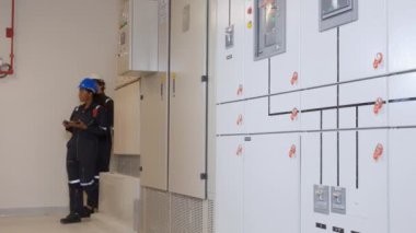 Electrical young woman and man engineer examining maintenance cabinet system electric in the control room at industrial factory, technician or electrician inspection power distribution.