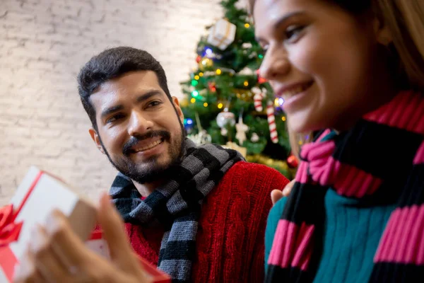 Young man giving presents for surprise girlfriend in celebration Christmas together at home, boyfriend giving gift woman with excited, event and festive x-mas, xmas and new year or holiday concept.
