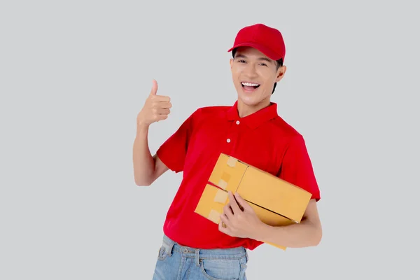 身穿制服的亚洲年轻人站着 头戴红帽子 提着箱子和大拇指竖起孤立的白色背景 员工拿着货物 快递和送货 运输和服务 物流和货物 — 图库照片