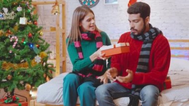 Genç bir kadın sürpriz erkek arkadaşına Noel 'i evde kutlarken hediyeler veriyor, kız arkadaşı da heyecanlı, olaylı ve şenlikli hediye kutlaması yapıyor, xmas ve yeni yıl ya da tatil konsepti..
