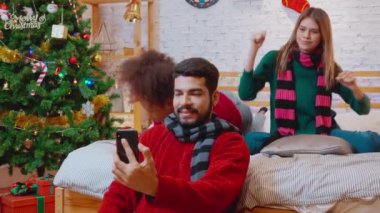 Genç arkadaşlar, Noel arifesinde, Noel arifesinde, Noel arifesinde, bayramında veya tatil konseptinde sosyal medyayı kullanan kadın ve erkek, heyecanlı ve akıllı telefonlardan keyif alarak görüntülü arama yaparlar..