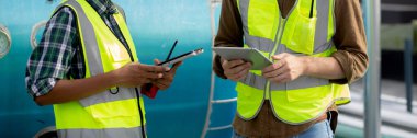 Young woman and man engineer examining pipeline and looking digital tablet in the factory, mechanic or technician inspector plumber valve and talking together, industrial and maintenance concept.