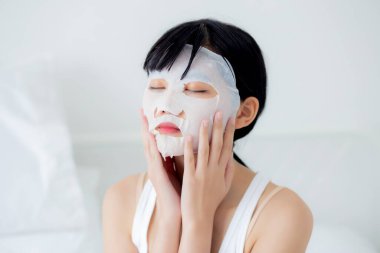 Yüzünde çarşaf maskesi olan güzel bir Asyalı kadın. Güzellik uzmanı. Yüzü kırışıklık, cilt bakımı, nemlendirici, sağlık ve sağlık için makyaj yapıyor..