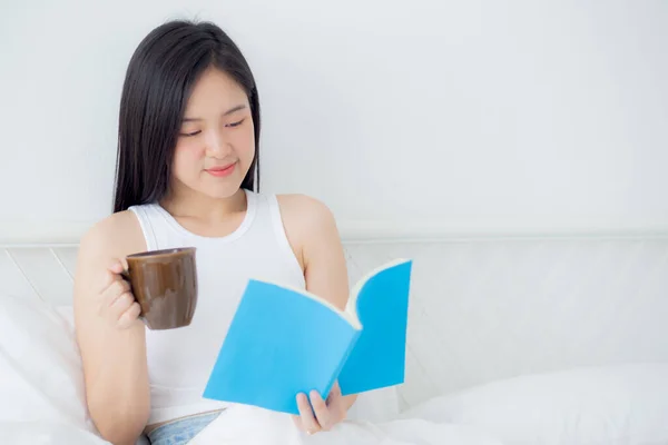 stock image Young asian woman reading a book and holding coffee glass with relax and cozy on the bed in the bedroom at home, female leisure reading novel while resting, one person, lifestyles concept.