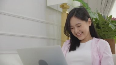 Young asian business woman work from home with laptop computer online to internet on sofa in living room, freelance girl using notebook sitting on couch with comfort and relax, lifestyles concept.