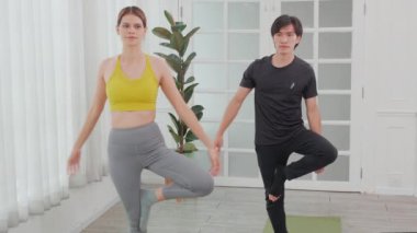 Genç bir kadın ve Asyalı erkek yoga yapıyor. Kasları esnek, bacakları ve elleri evde. Vücut bakımı için yoga, vücut esnekliği, spor ve sağlık konsepti ile rehabilitasyon yapıyor..