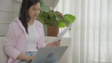 Young asian business woman working on laptop computer and looking graph and chart of report for profit on paper at home, businesswoman looking investment and income, data of infographic statistics.