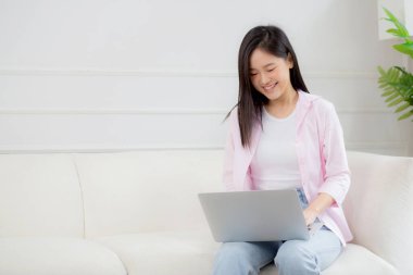 Young asian business woman work from home with laptop computer online to internet on sofa in living room, freelance girl using notebook sitting on couch with comfort and relax, lifestyles concept.