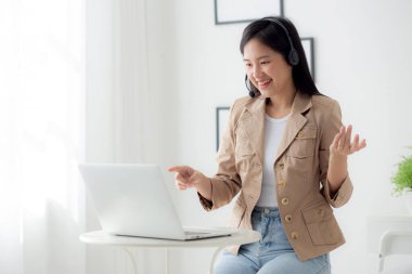 Young asian businesswoman wearing headset video call and explain conference online at home, woman wearing headphone meeting and talking for working from home, business and communication concept.