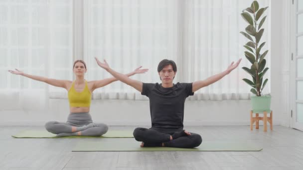 若いアジアの男性と女性はヨガを練習し 自宅でマットの上でリラックスしてバランスのとれた生活のための瞑想 カップルが座ってトレーニングヨガの練習 健康とスポーツの概念 — ストック動画