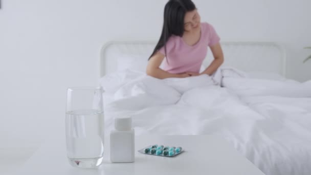 若いアジアの女性は 病気の便秘や自宅で寝室で消化不良 不幸な女性の病気や月経や胃 医療や健康の概念でベッドの痛みの胃や腸に座って — ストック動画