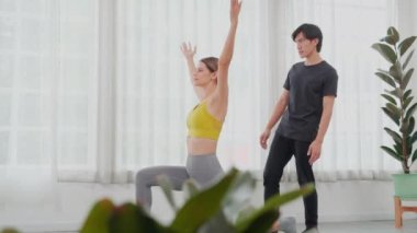 Genç Asyalı antrenör, evde el ve dengesini korurken yoga yapan kadını eğitiyor. Kadın eğitmen, temel, sağlık ve spor konseptiyle egzersiz yogasında yardımcı oluyor..