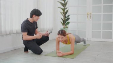Genç kadın, duruş tahtası ile antrenman yaparken, Asyalı erkek antrenör evde mücadele, egzersiz ve antrenman için kararlılık zamanını sağlık, spor konsepti ve özveri ile değerlendiriyor..
