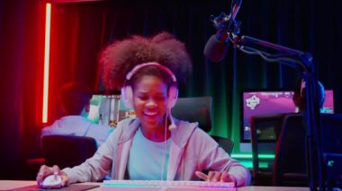Genç Afro-Amerikan kadın ve takımı kulaklık takarak video oyunu oynuyor ve canlı yayında mikrofon, oyun ve esport ile rekabet veya oyuncu seçimi, yayın ve eğlence kavramı ile çevrimiçi olarak yayınlanıyor..