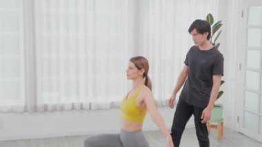 Genç Asyalı antrenör, evde el ve dengesini korurken yoga yapan kadını eğitiyor. Kadın eğitmen, temel, sağlık ve spor konseptiyle egzersiz yogasında yardımcı oluyor..