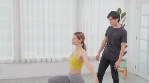 在家里 年轻的亚洲教练训练女子练瑜伽 同时伸出手来 在房间里保持平衡 教练帮助女子练习基本的 健康的和运动的瑜伽 — 图库视频影像