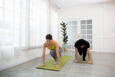 Yoga yapan genç adam ve kadın ve kaslı eller evdeki paspasın üzerinde birlikte sağlık için geriniyorlar. Vücut esnekliği, spor konsepti ve vücut esnekliği için çift yoga eğitimi yapıyorlar..