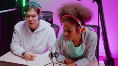 Genç Afrikalı Amerikalı kadın ve Asyalı erkek stüdyoda canlı yayında röportaj ve sohbet, erkek ve kadın sunucu kulaklık takarak mikrofon, radyo ve yayın konseptiyle konuşuyor..