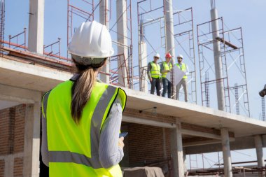 Young caucasian woman engineer command and control labor or coworker while looking blueprint on construction site, architect or contractor control and planning development structure house.