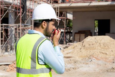 Young man engineer using radio command with worker in construction site, architect or contractor speak to radio for control and planning development structure house, foreman or supervisor.