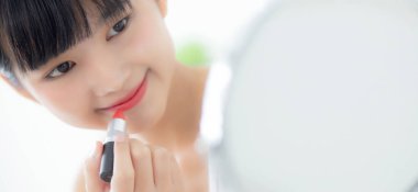 Güzel, genç Asyalı bir kadın dudaklarına ruj sürüyor, dudaklarına kırmızı ruj sürüyor, güzellik kızı makyaj malzemesi için aynaya bakıyor, zarif dudaklarıyla makyaj yapıyor, seksi bir kadın, cilt bakımı ve sağlık konseptiyle barışıyor..