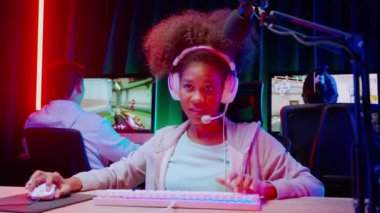 Genç Afro-Amerikan kadın ve takımı kulaklık takarak video oyunu oynuyor ve canlı yayında mikrofon, oyun ve esport ile rekabet veya oyuncu seçimi, yayın ve eğlence kavramı ile çevrimiçi olarak yayınlanıyor..