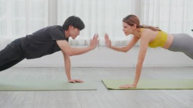Genç kadın ve Asyalı erkek, motivasyon ve kararlılıkla evde ağırlık antrenmanı yaparken paspasın üzerinde tahtayla antrenman yapıyorlar. Kadın ve erkek, güçlü ve güçlü bir spor konseptiyle ağırlık antrenmanı yapıyorlar..