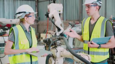 Mühendis erkek ve kadın robot silahları hakkında konuşuyor ve anlatıyor. Teknoloji zekası ve yenilik fabrikada, geliştirme makinesi robotu, insanlar makine elektronik, endüstri konseptini inceliyor..