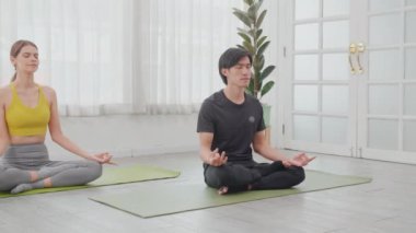 Young asian man and woman practicing yoga and meditating for relaxation and balance life on mat in room at home, female and male sitting and training workout yoga exercise, health and sport concept.
