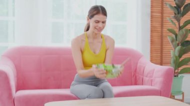 Evdeki oturma odasında marul yediği için kasede salata sebzesi, sağlıklı beslenme, yaşam tarzları ve sağlık konsepti için kadın ve vejetaryen yemekleri tutan mutlu beyaz kadın..