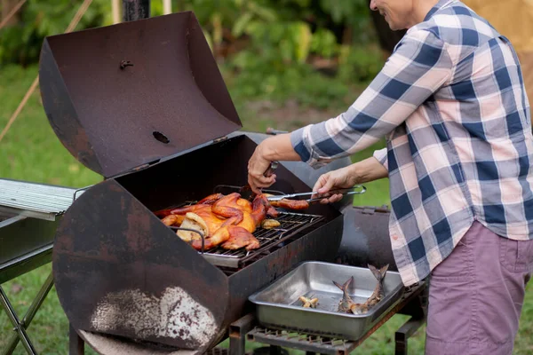 Senior woman grilling chicken meat for preparing eat in camping, elderly doing activity recreation and leisure picnic while roasting meat in weekend, travel trip in holiday, party in vacations.