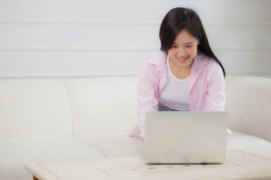 Genç Asyalı iş kadını evde dizüstü bilgisayarla çalışıyor oturma odasındaki kanepede internete bağlanıyor, defter kullanan serbest bir kız rahat ve rahat bir şekilde kanepede oturuyor, yaşam tarzı kavramı..