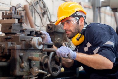 Genç Kafkasyalı mühendis, fabrika endüstrisinde, teknisyen veya işgücü bakım makinelerinde üretimi hazırlamak için torna makinesini çalıştırıyor..