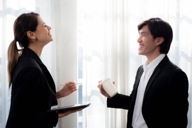 Young manager standing and talking with secretary about report marketing on digital tablet with relax and laughing at office, colleague discussion with friendship together, business concept.