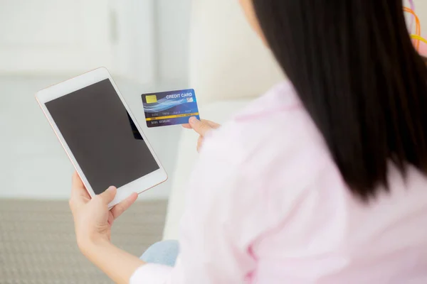 Young asian woman holding credit card shopping online with tablet computer blank display screen buying and payment, female using debit card purchase or transaction, business and ecommerce concept.