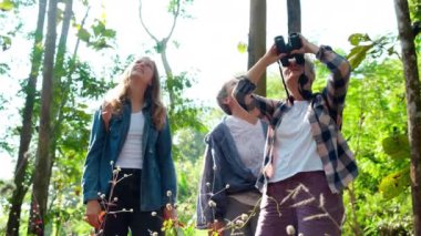 Teenager girl and two grandmother traveling travel to forest and adventure while using binoculars exploration together with happy, senior woman and granddaughter hiking with fun and vitality.