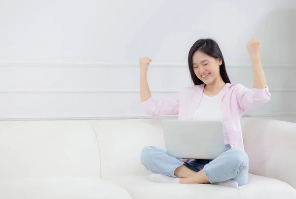 stock image Happiness young asian woman sitting on sofa and working on laptop computer while successful and excitement at home, freelance female using notebook and achievement, business and lifestyles concept.