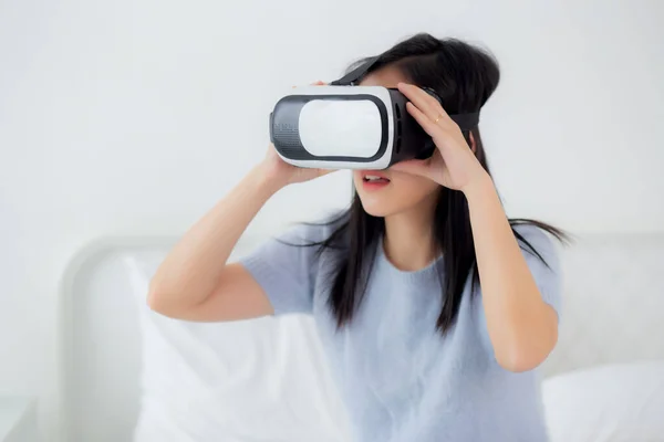 stock image Young asian woman wearing vr headset playing game with excited on bed in the bedroom at home, female using virtual reality or metaverse innovation for simulation 3D, lifestyles and technology concept.