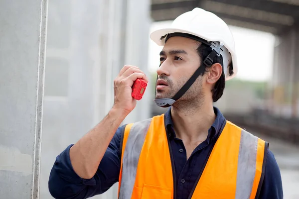 Young man engineer using radio command with worker in construction site, architect or contractor speak to radio for control and planning development structure at precast factory, industrial concept.