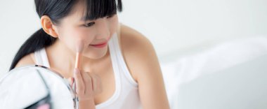 Laptop bilgisayarında yanağına fırça sürerek makyaj yapmayı öğrenen genç Asyalı bir kadın. Yatakta özel ders veren, öğretmenlik yapan ve sosyal medyada makyaj yapan bir kadın..