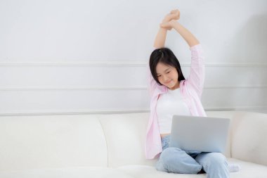 Beautiful young asian businesswoman sitting on sofa and working from home and break while stretch arm for relax in living room at home, woman is freelance working on laptop computer, business concept.