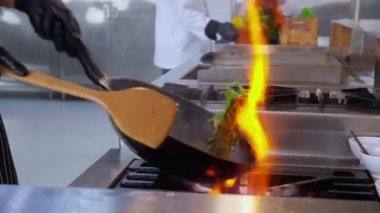 Şefin yakın elleri, sabah alevini, restoranda yanan tavayla, yemek ve besinle, yavaş çekimde yemek pişirme, aşçılık ve yemek tarifi ile karıştırıyor..